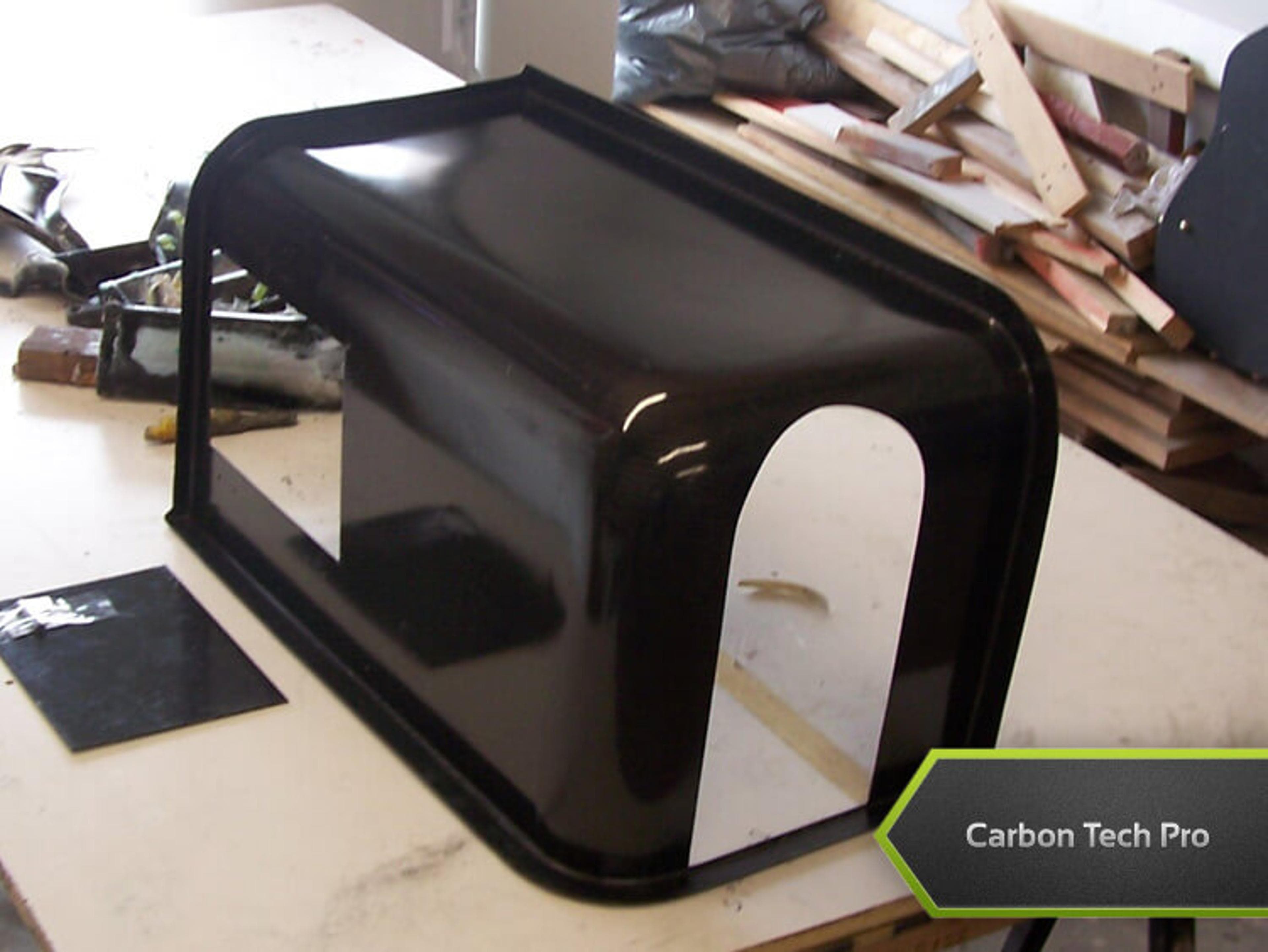 "Smooth, high-gloss carbon composite housing built for custom aerospace applications. Glossy black molded housing component with cutouts resting upside down on a table.