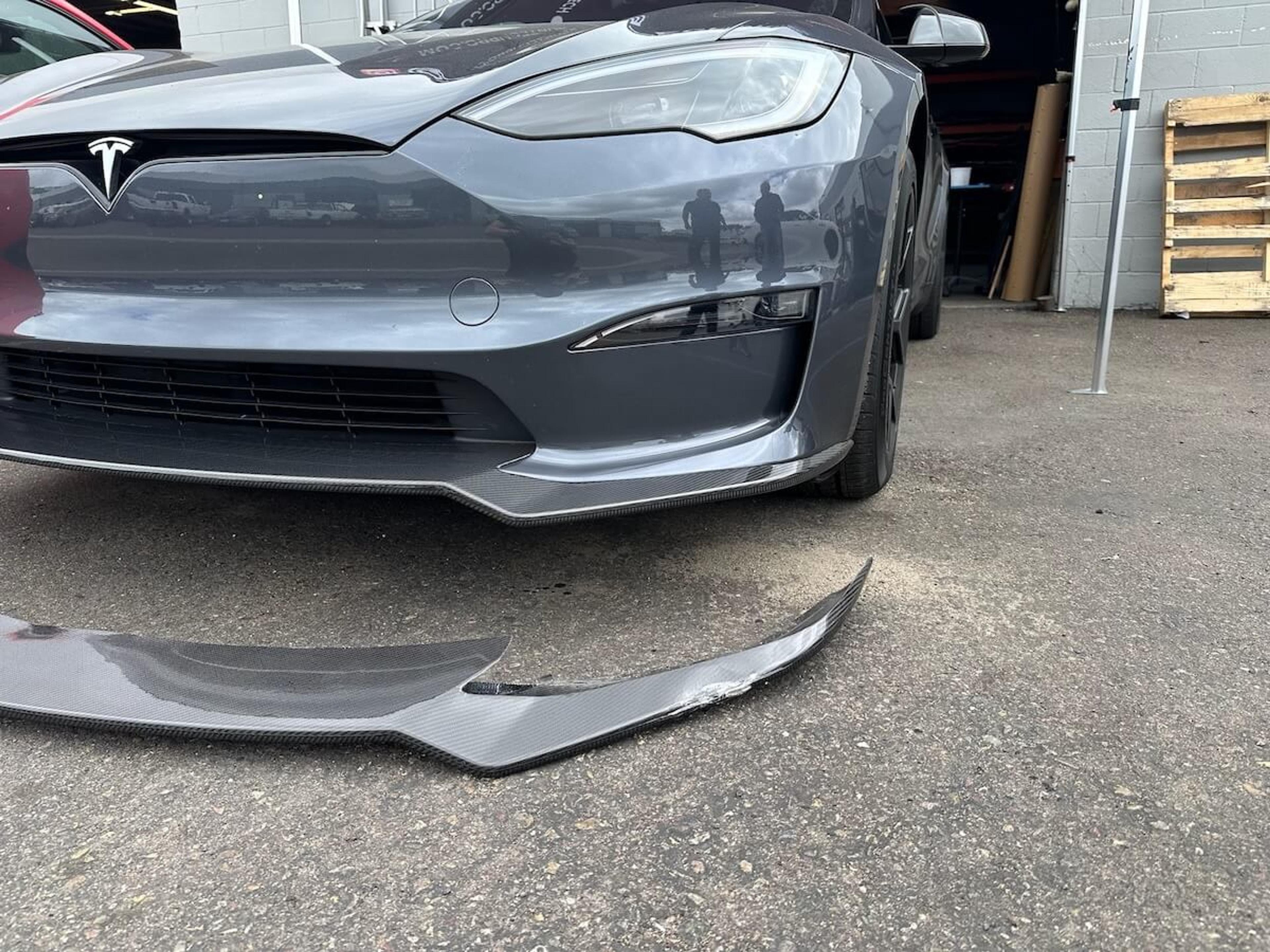 Damaged front lip removed for replacement Tesla Model Y with damaged carbon fiber front lip removed and placed in front of the vehicle