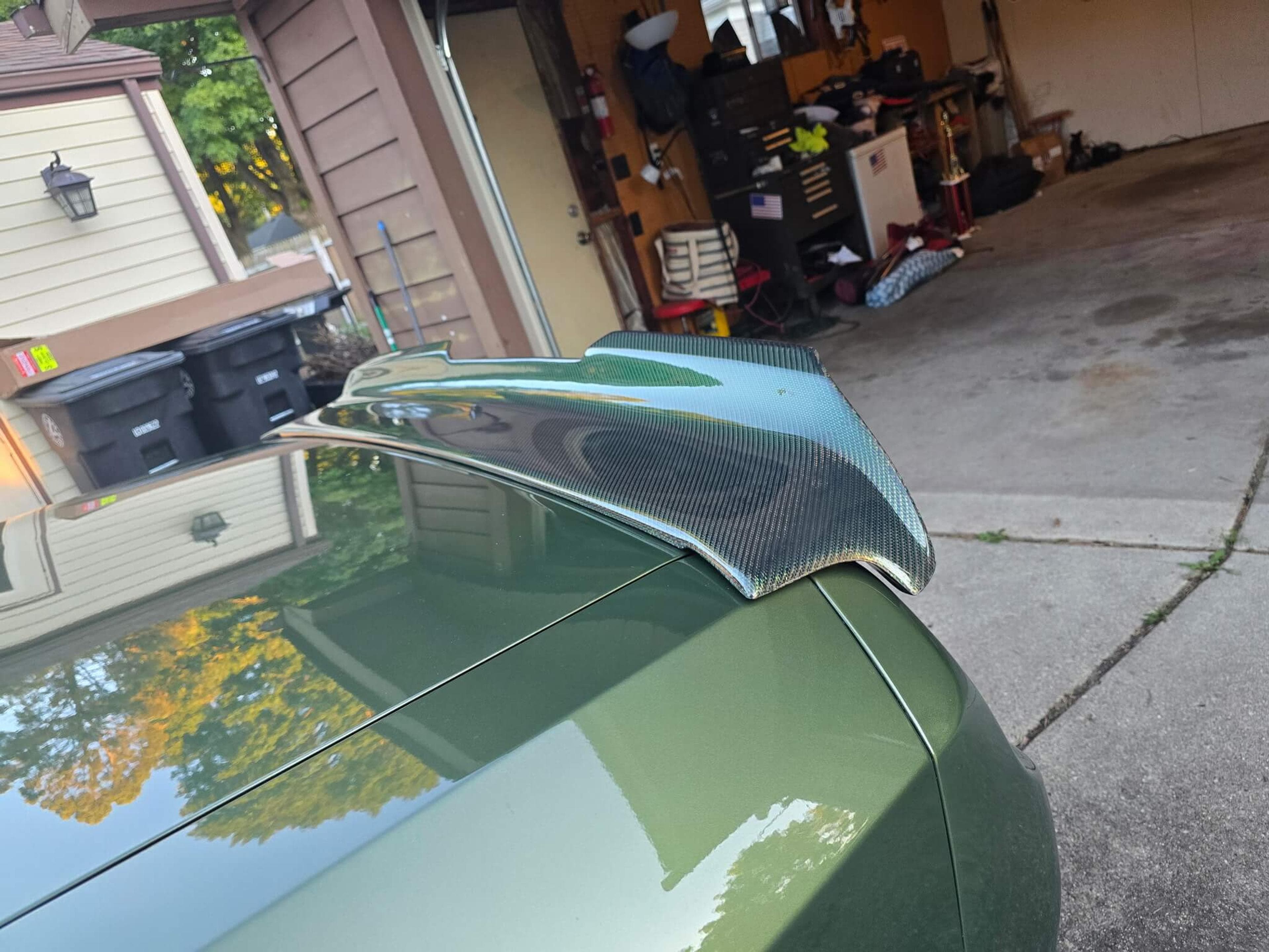 Dodge Challenger carbon fiber spoiler side profile Rear-side view of a green Dodge Challenger showing its carbon fiber spoiler and matching fuel door.