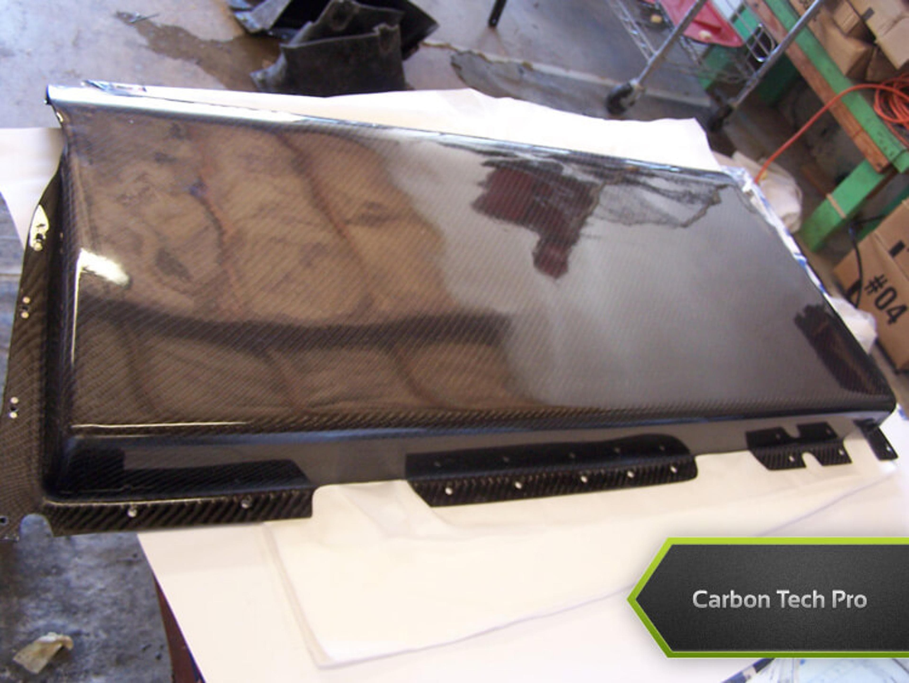 High-gloss woven carbon fiber panel fresh off the production line. High-gloss carbon fiber panel laying flat on a white padded surface in a workshop
