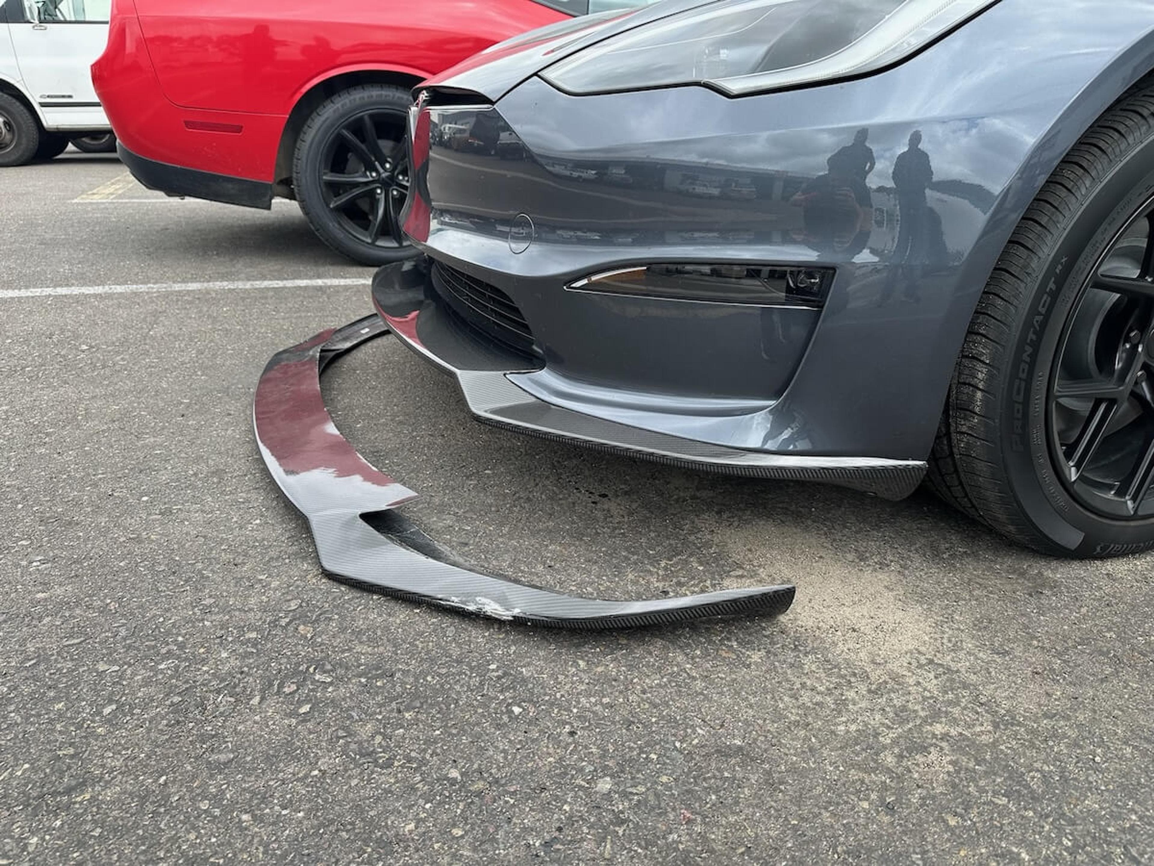 Original damaged carbon fiber front lip Damaged carbon fiber front lip beside the front bumper of a gray Tesla Model Y