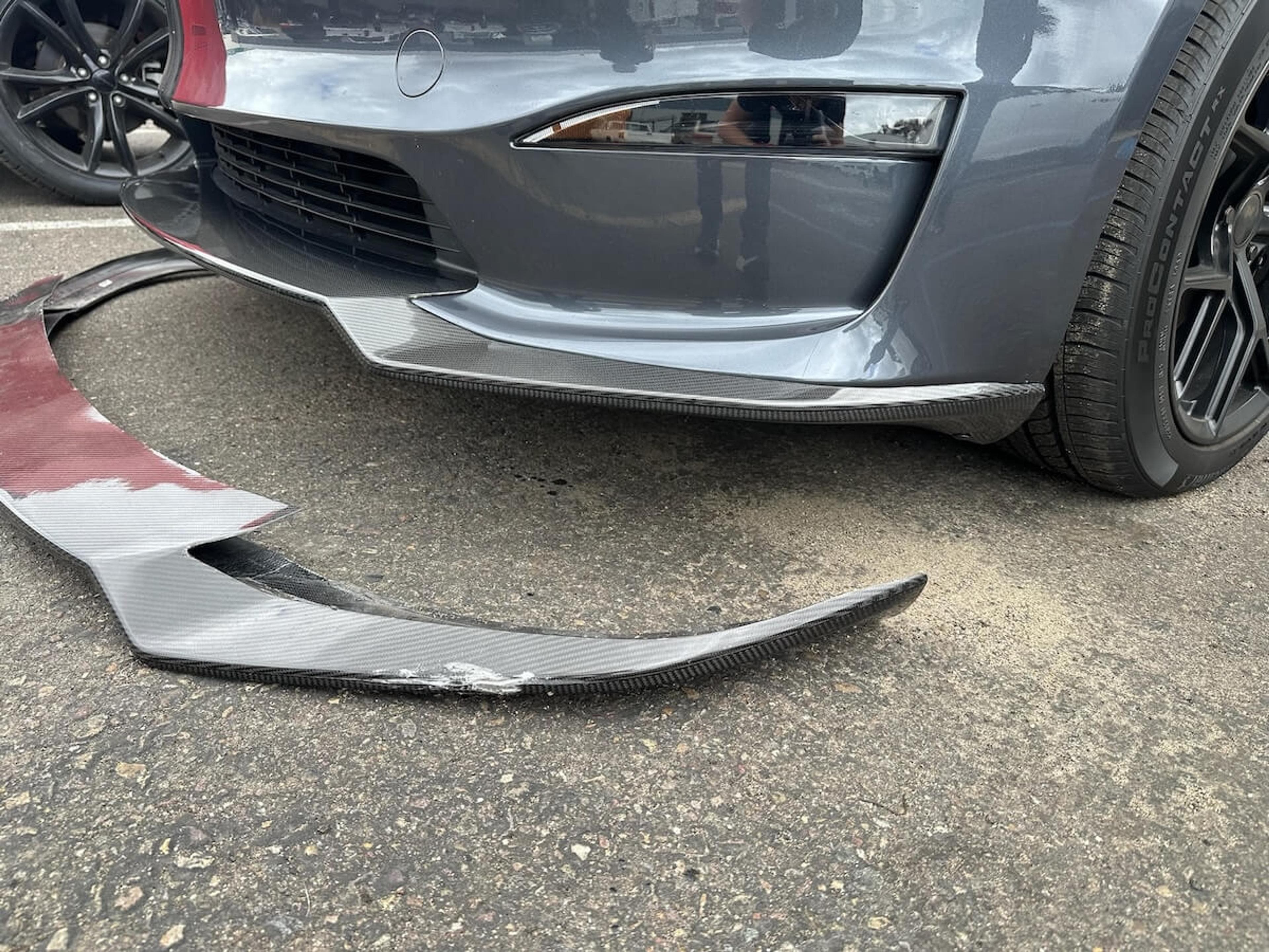Close-up of the damaged front lip before replacement Close-up of damaged carbon fiber Tesla Model Y front lip next to the installed replacement